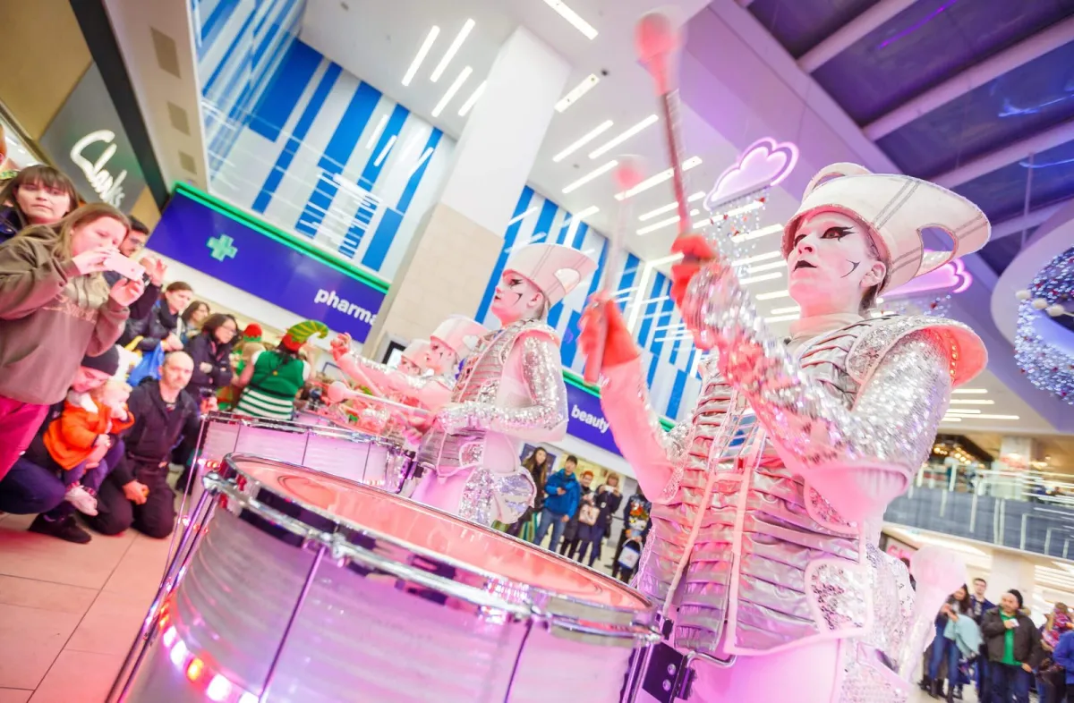 Spark! performers in pink and silver drumming in a busy shopping centre at Christmas.
